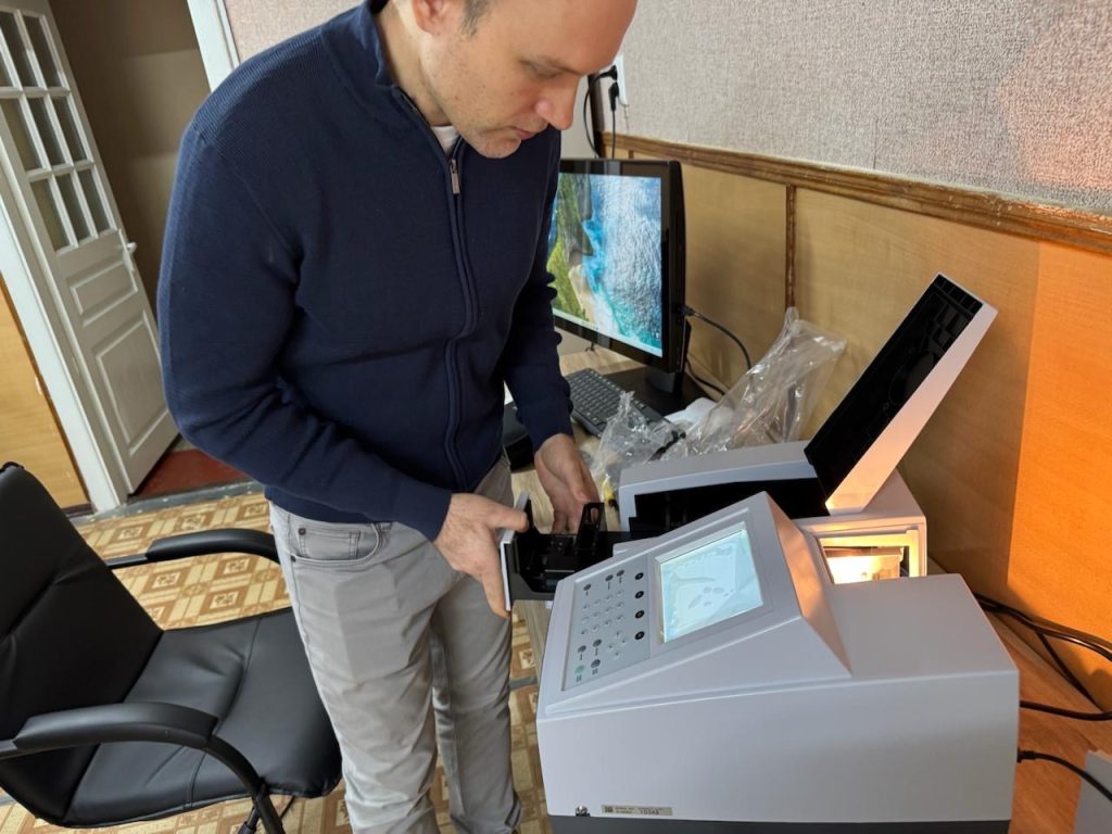 A participant adjusts the open sample compartment of a Shimadzu UV-1280 spectrophotometer during equipment training at KSAEU.